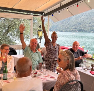 Un gruppo di persone sedute al tavolo su una terrazza con vista lago con bicchieri da vino